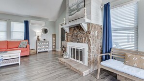 A living room with a stone fireplace, a sofa, a coffee table, and a bench. - The Showboat 3 Bedroom Home (Port Bolivar)
