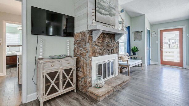 A living room with a stone fireplace, a mounted television, and a door leading to another room. - The Showboat 3 Bedroom Home (Port Bolivar)