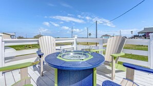 A deck with a hot tub, two Adirondack chairs, and a view of the beach. - The Showboat 3 Bedroom Home (Port Bolivar)