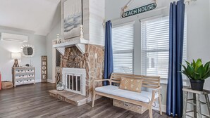 A living room with a stone fireplace, a wooden bench, a potted plant, and a sign reading 'BEACH HOUSE'. - The Showboat 3 Bedroom Home (Port Bolivar)