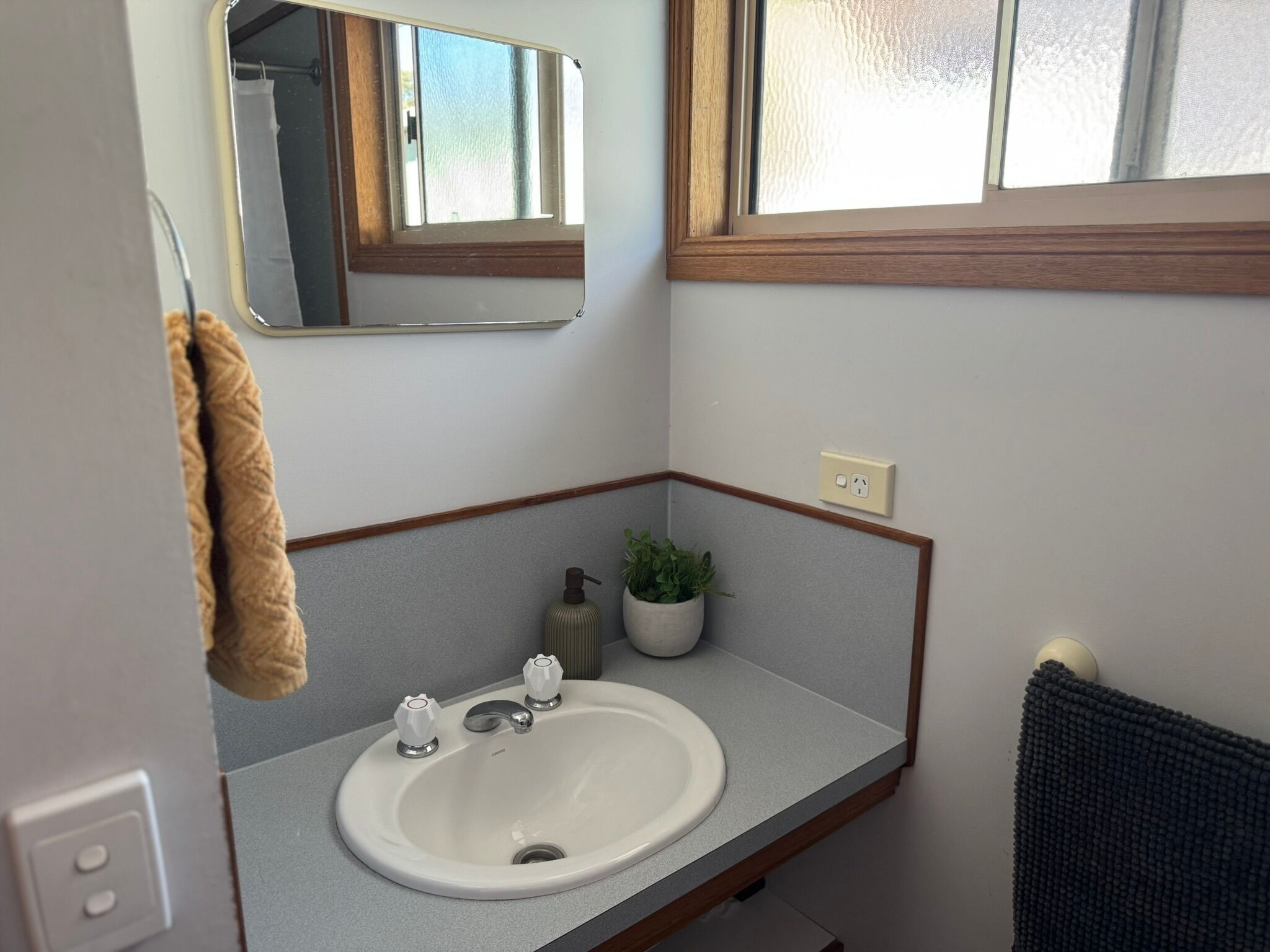 Ein Badezimmer mit einem weißen Waschbecken, einem Spiegel, einem Fenster und einem Handtuch an der Wand.