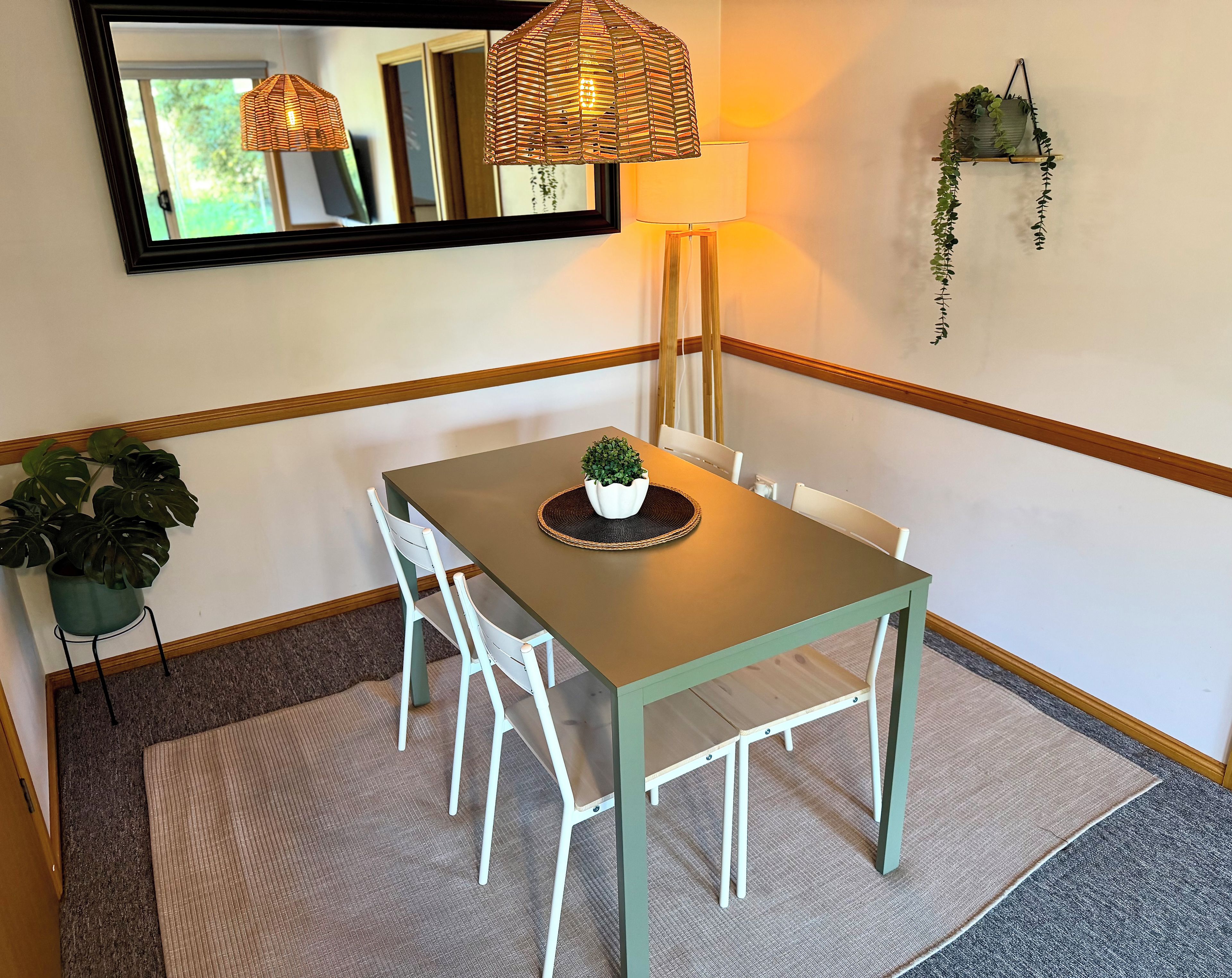 Un espace repas comprenant une table, des chaises, un luminaire suspendu, un miroir et une plante en pot.