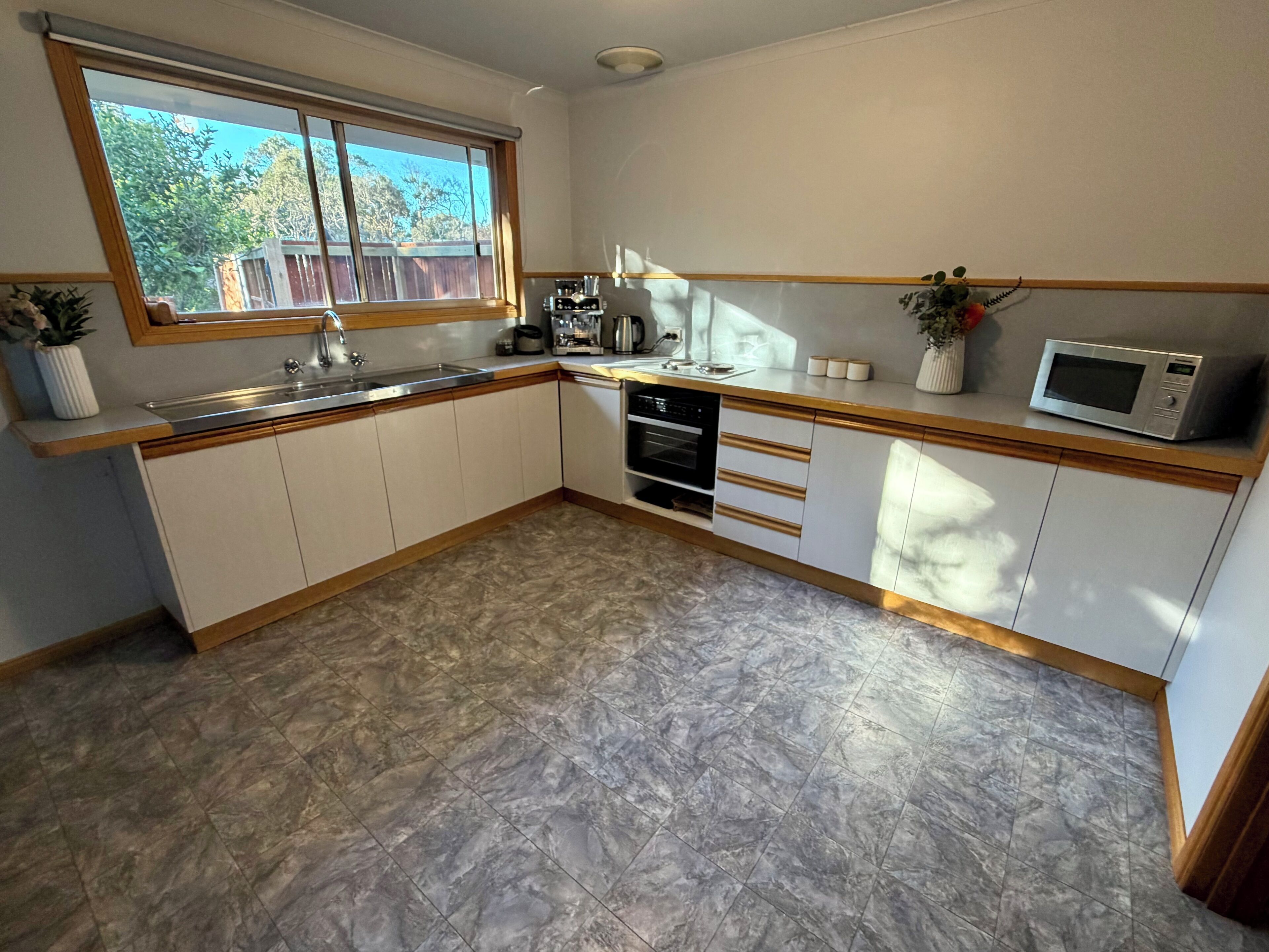 Une cuisine avec une fenêtre, un évier, des placards, un four à micro-ondes et une cuisinière.