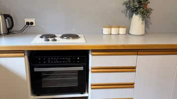 Uma cozinha com forno embutido, chaleira e pequeno balcão com uma planta, açúcar e recipientes para chá.