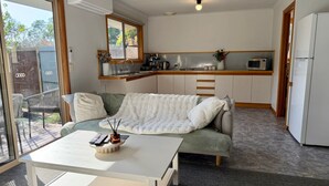 Un espacio habitable compacto con sofá, una mesita, kitchenette y puerta corrediza de vidrio que da a un área exterior.