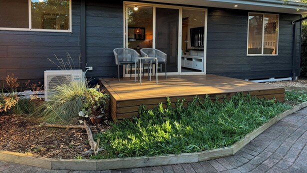 A modern house with a deck, two chairs, and a TV.