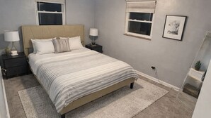 Ein Schlafzimmer mit Bett, Nachttischen, Teppich, Fenster und einem Wandbild.