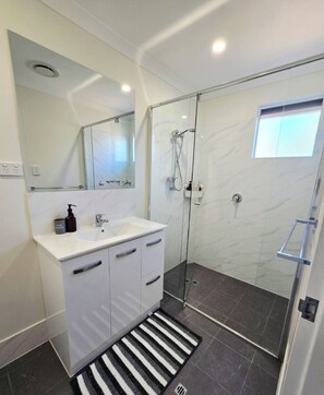 Casa de banho moderna com cabine de chuveiro em vidro, toucador branco com espelho e tapete listrado a preto e branco.
