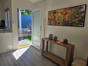Um interior moderno com uma porta de correr de vidro que dá para um pátio, uma mesa consola com objetos decorativos e uma pintura abstrata colorida na parede.