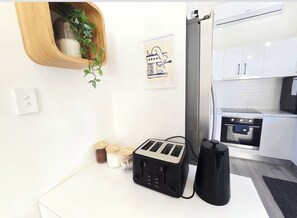 Uma cozinha moderna com armários brancos, uma torradeira, uma chaleira e um eletrodoméstico preto sobre o balcão.