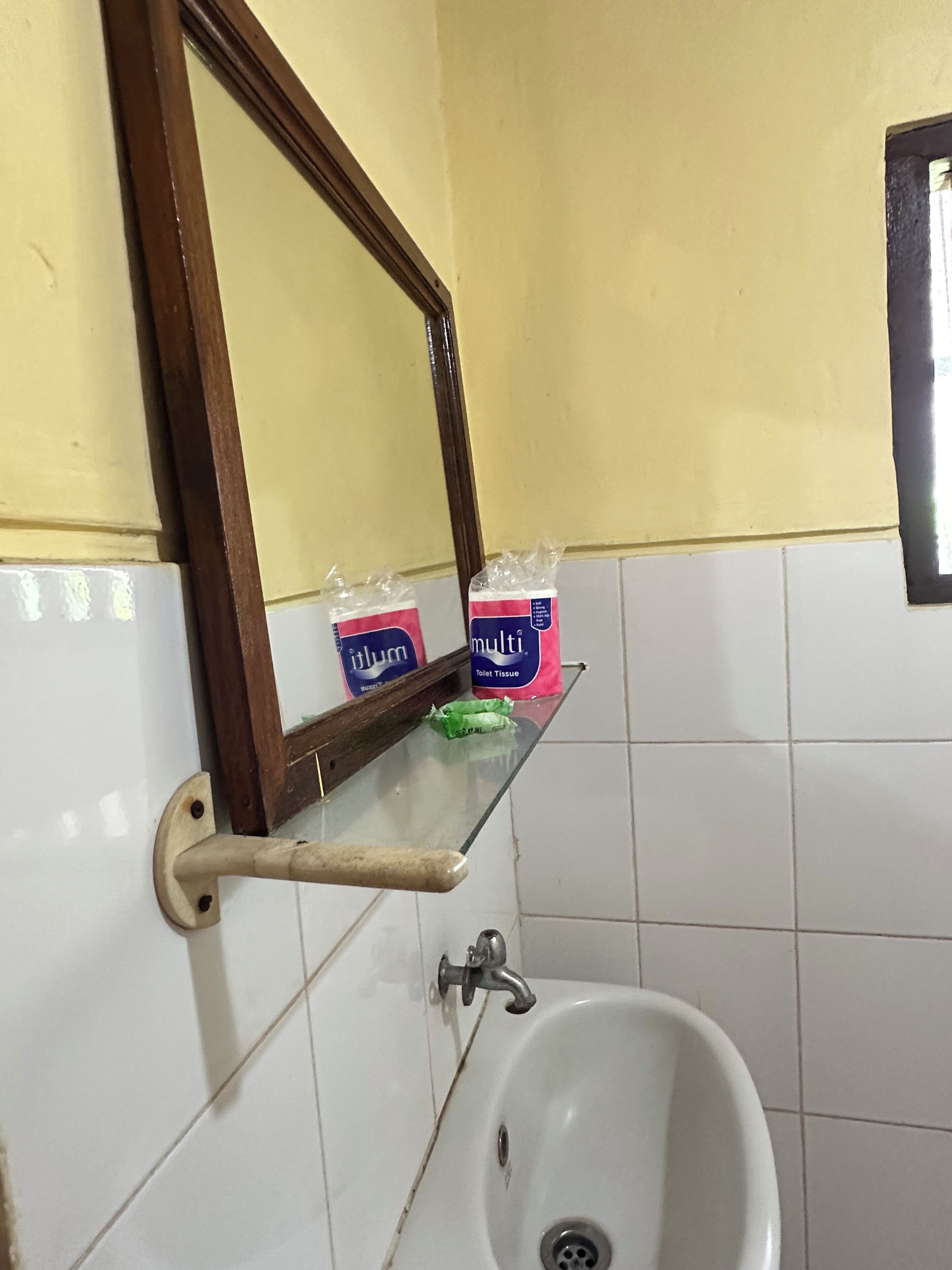 Ein Badezimmer mit einem weißen Waschbecken, einem Spiegel und zwei Toilettenpapierrollen auf einem Regal.