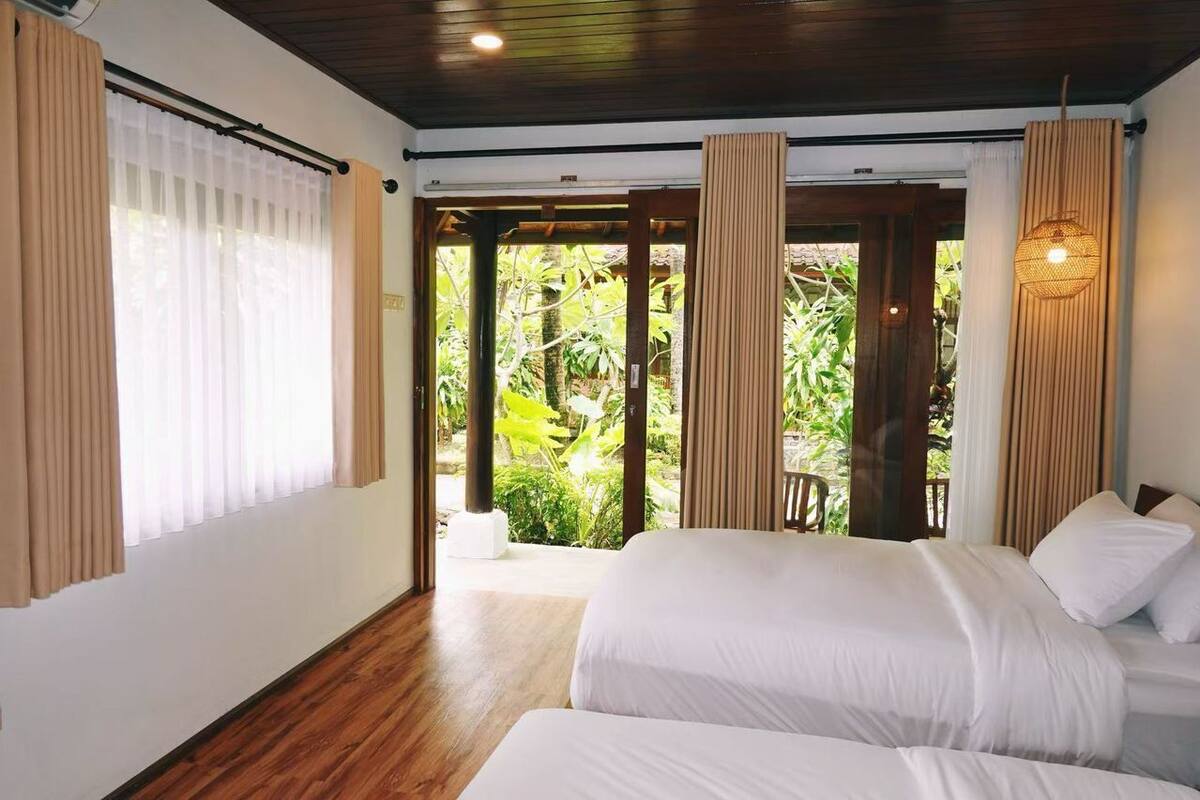 Ein Schlafzimmer mit einem großen Bett, Holzboden und Blick auf Grün hinter der Tür.