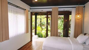 A bedroom with a bed, curtains, and a view of greenery outside. - Paradise Palm Beach Bungalows and Dive Center (Tulamben)