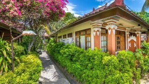 A traditional house with a tiled roof, surrounded by lush greenery and a pathway leading to the entrance. - Paradise Palm Beach Bungalows and Dive Center (Tulamben)