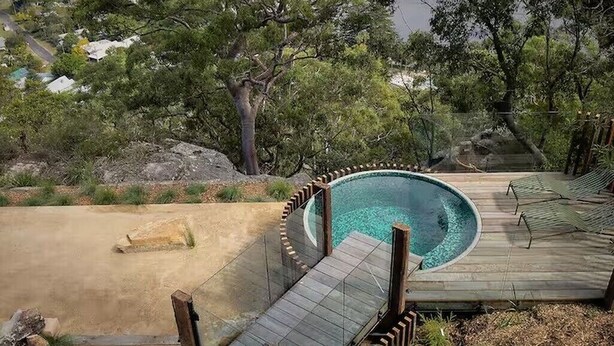 A swimming pool with a wooden deck, surrounded by trees and a sandy area. - Patonga House: Stunning Views, Privacy, Heated Pool and Panoramic Outdoor Sauna (Patonga)