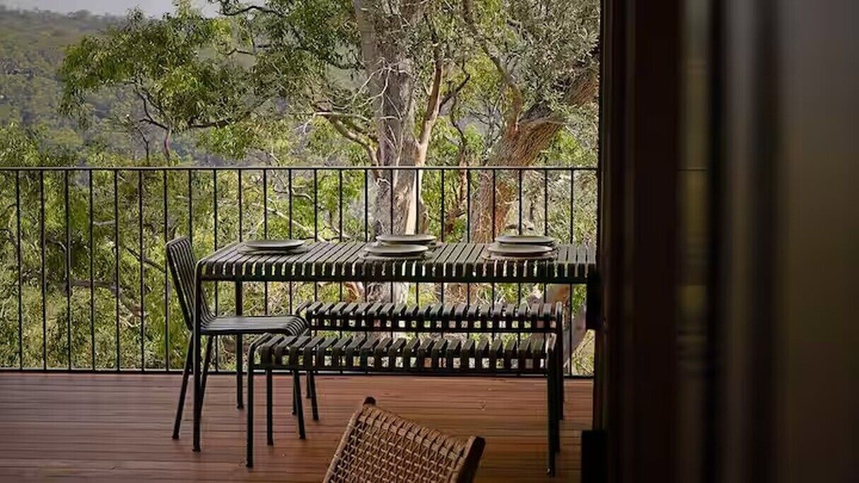 Een balkon met een tafel en stoelen, met uitzicht op een bebost landschap.
