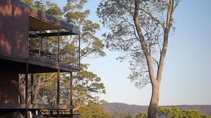 A two-story building with a balcony, surrounded by trees and a clear sky. - Patonga House: Stunning Views, Privacy, Heated Pool and Panoramic Outdoor Sauna (Patonga)