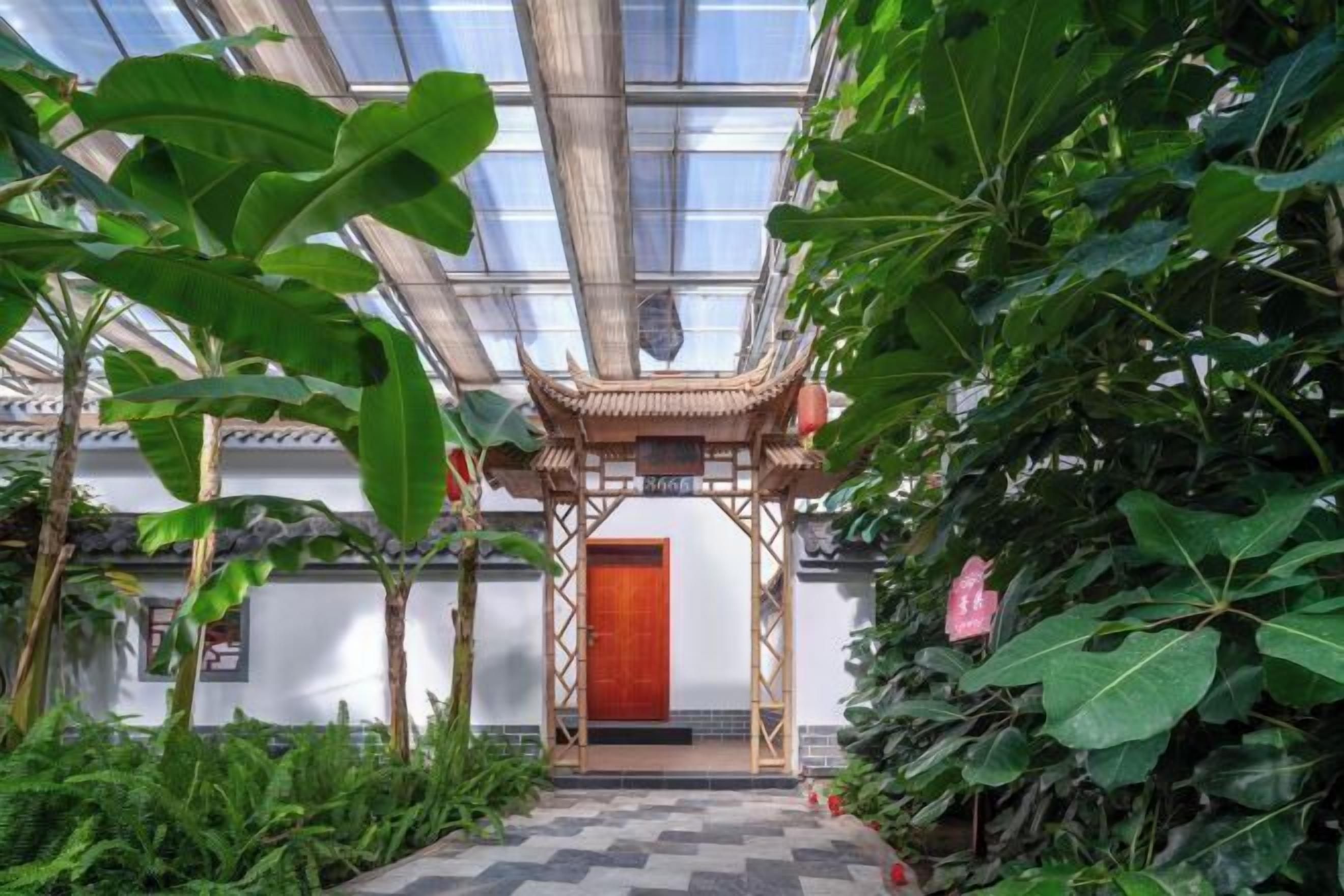 Estructura arquitectónica tradicional con tejado de madera y puerta roja, rodeada de abundante vegetación.