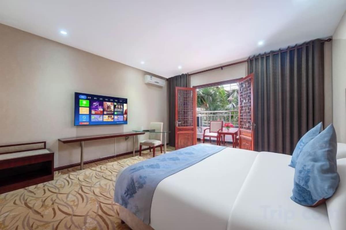 A hotel room with a bed, a desk, a television, and a balcony with a view of the outdoors.