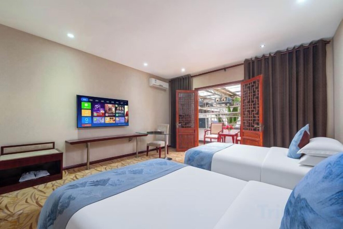 A hotel room with two beds, a TV, a desk, and a balcony with a view.