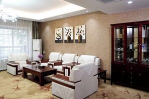A hotel room with a sofa set, a coffee table, a cabinet with glass doors, and artwork on the wall.