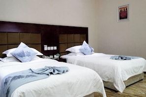 A hotel room with two beds, each with a headboard and pillows.