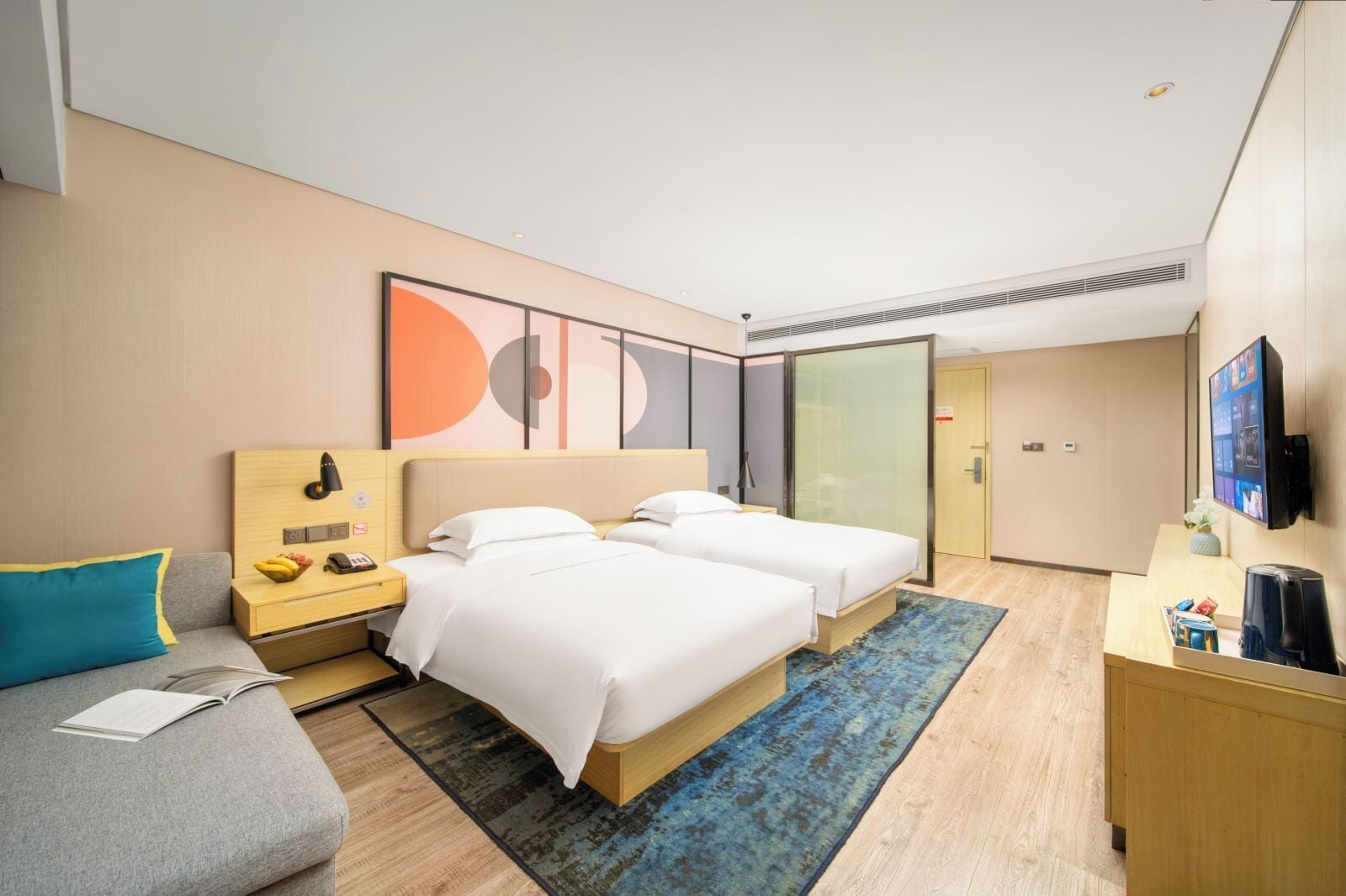 Habitación de hotel con dos camas, un escritorio con ordenador, televisor y un pequeño rincón de descanso.