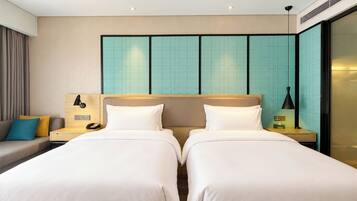 A hotel room with two beds, a sofa, a nightstand with a lamp, and a wall with a grid pattern.
