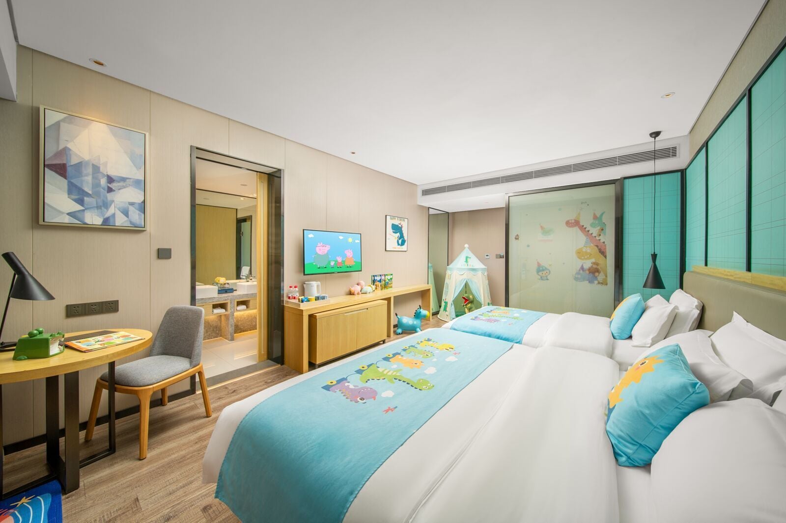 Une chambre d’hôtel équipée d’un lit, d’un bureau, d’une chaise, d’une télévision et d’un espace de jeux pour enfants.