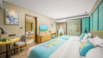A hotel room with a bed, desk, chair, TV, and children's play area.