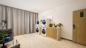 A modern hotel room with a large window, a sofa, a desk, a washing machine, a sink, and a door. - Yishang Hotel Kunming Changshui Airport (Kunming)