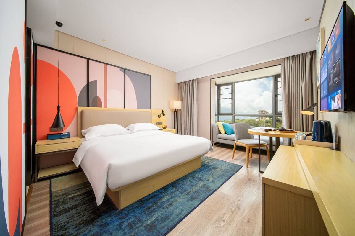A hotel room with a bed, a desk, a chair, a TV, and a large window.