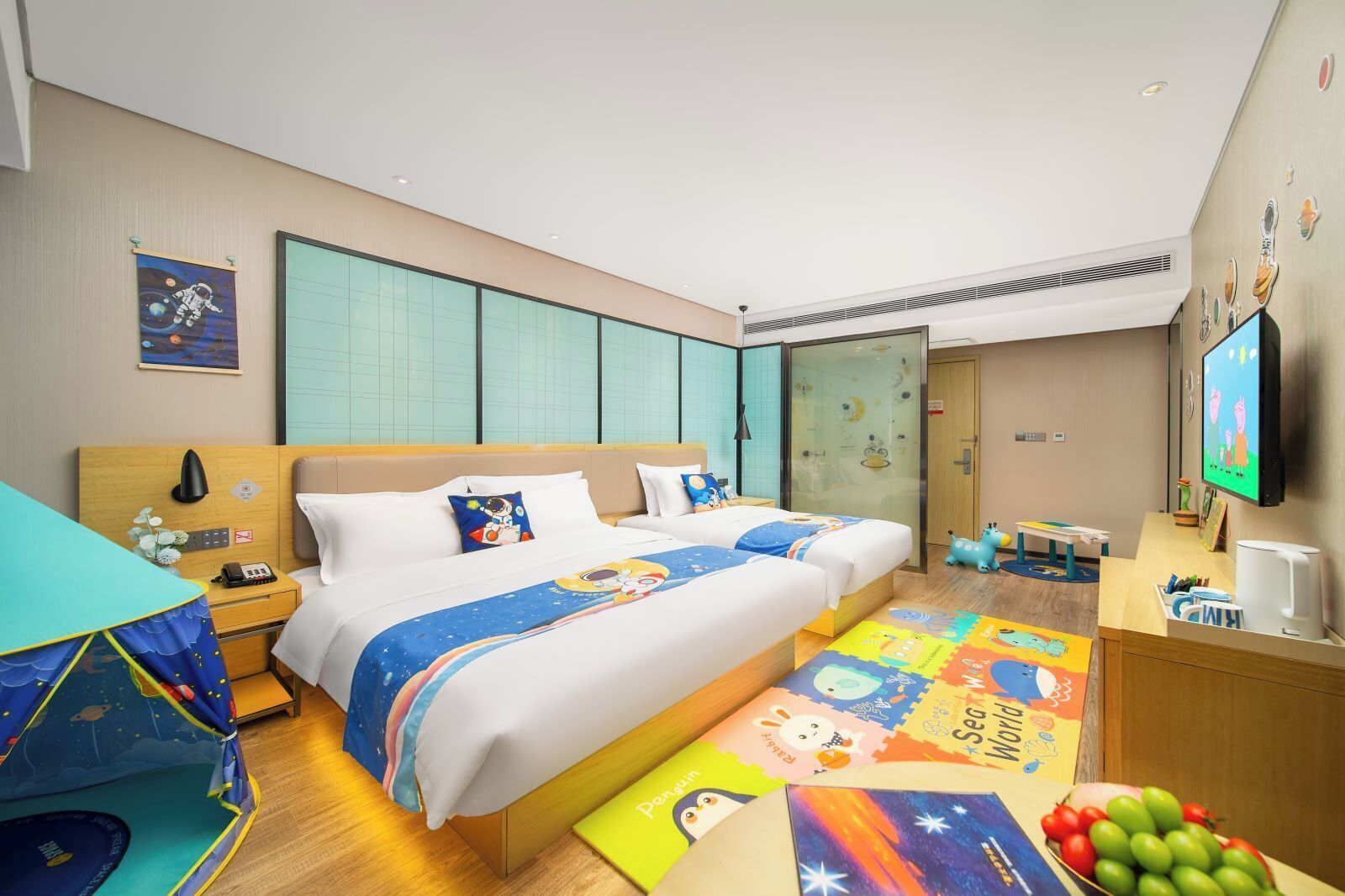 Ein Hotelzimmer mit einem großen Bett, einem Schreibtisch, einem Fernseher und einem Spielbereich für Kinder.