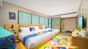 Ein Hotelzimmer mit einem großen Bett, einem Schreibtisch, einem Fernseher und einem Spielbereich für Kinder.