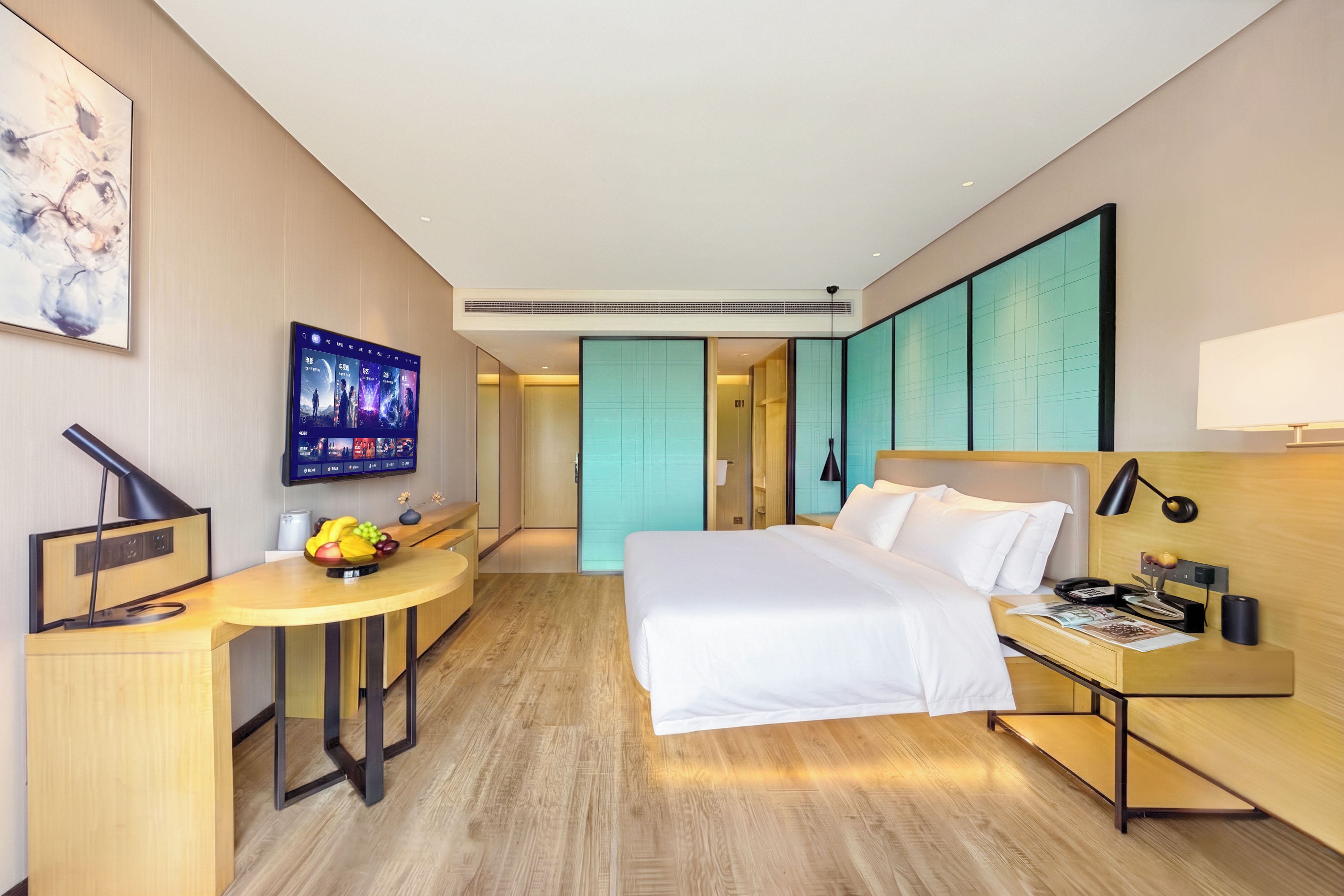 Moderni hotellihuone, jossa on sänky, työpöytä ja televisio, jolla näkyy elokuvajulisteita.
