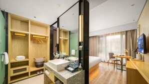 A modern hotel room with a large bed, a sitting area with a table and chair, a bathroom with a vanity and mirror, and a television mounted on the wall. - Yishang Hotel Kunming Changshui Airport (Kunming)