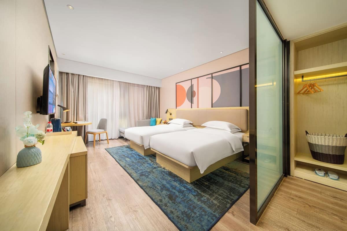 A hotel room with a bed, desk, chair, TV, and a large window with curtains.