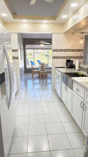 A modern kitchen with white cabinets, a dishwasher, and a dining area with a table and chairs. -   Peaceful Rotonda West Retreat Near Beaches & Golf (Rotonda West)