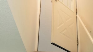 Un escalier dont les marches sont recouvertes de moquette, menant à une porte blanche dotée d’un panneau de verre.