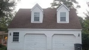 Une maison à deux étages, avec un toit à pignon, deux portes de garage et une petite fenêtre au premier étage.