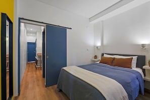 A bedroom with a bed, bedside table, and a door leading to another room.