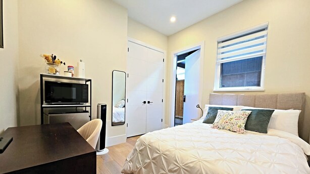A bedroom with a bed, a desk, a TV, and a mirror.