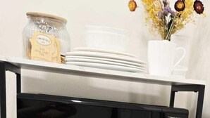 A kitchen area with a microwave on a black and white stand, a refrigerator below, and a jar of tea on the counter.