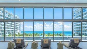 A hotel room with large windows overlooking a beach and ocean, featuring lounge chairs and a tropical view. - Confirmed Reservation in Cancun!Thanksgiving Week!   (Cancún)