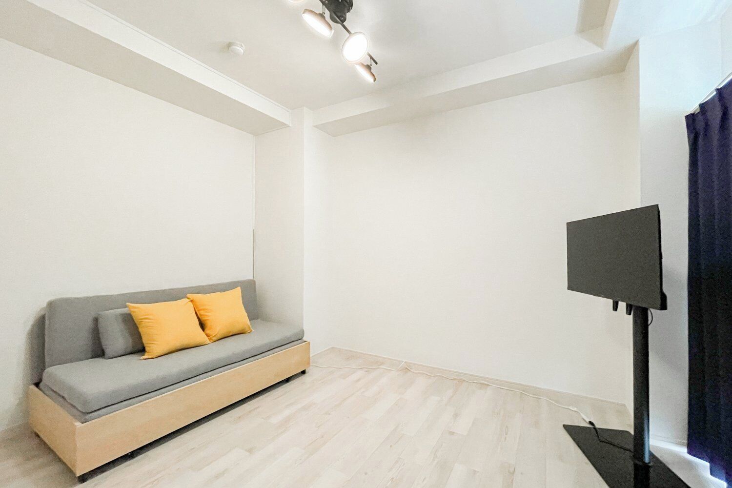A modern room with a grey sofa, yellow cushions, a flat-screen TV, and a wooden floor.