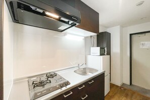 A compact kitchen with a gas stove, a sink, and a microwave on a white countertop. - Osaka House Honkan (Osaka)