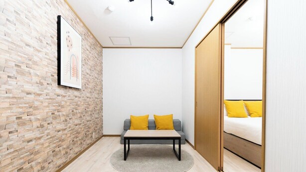 Ein Zimmer mit einer Ziegelwand, einem grauen Sofa mit gelben Kissen, einem kleinen Tisch und einem Bett mit gelben Kissen.