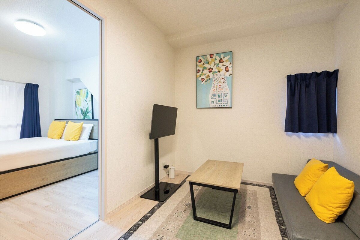 A hotel room with a bed, a desk, a sofa, a TV, and a painting on the wall.