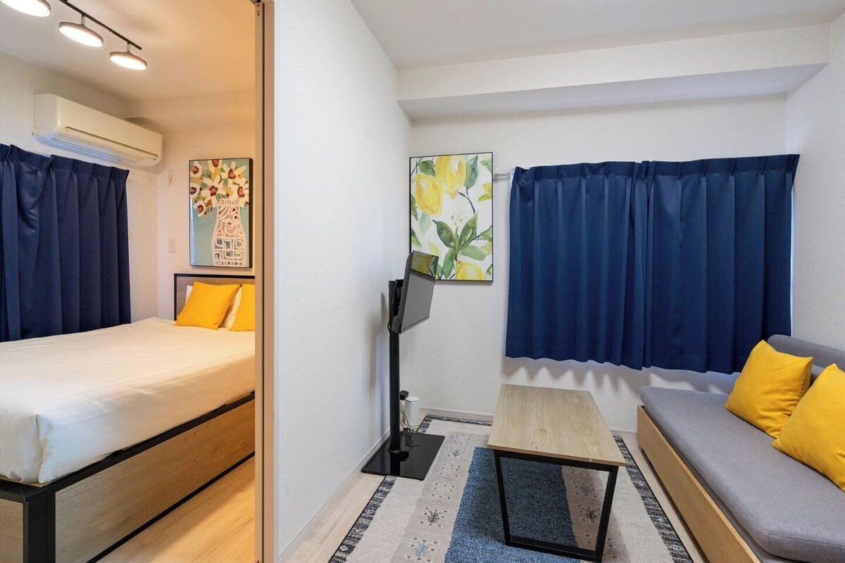 A compact hotel room with a bed, a sofa, a small table, and two paintings on the wall.