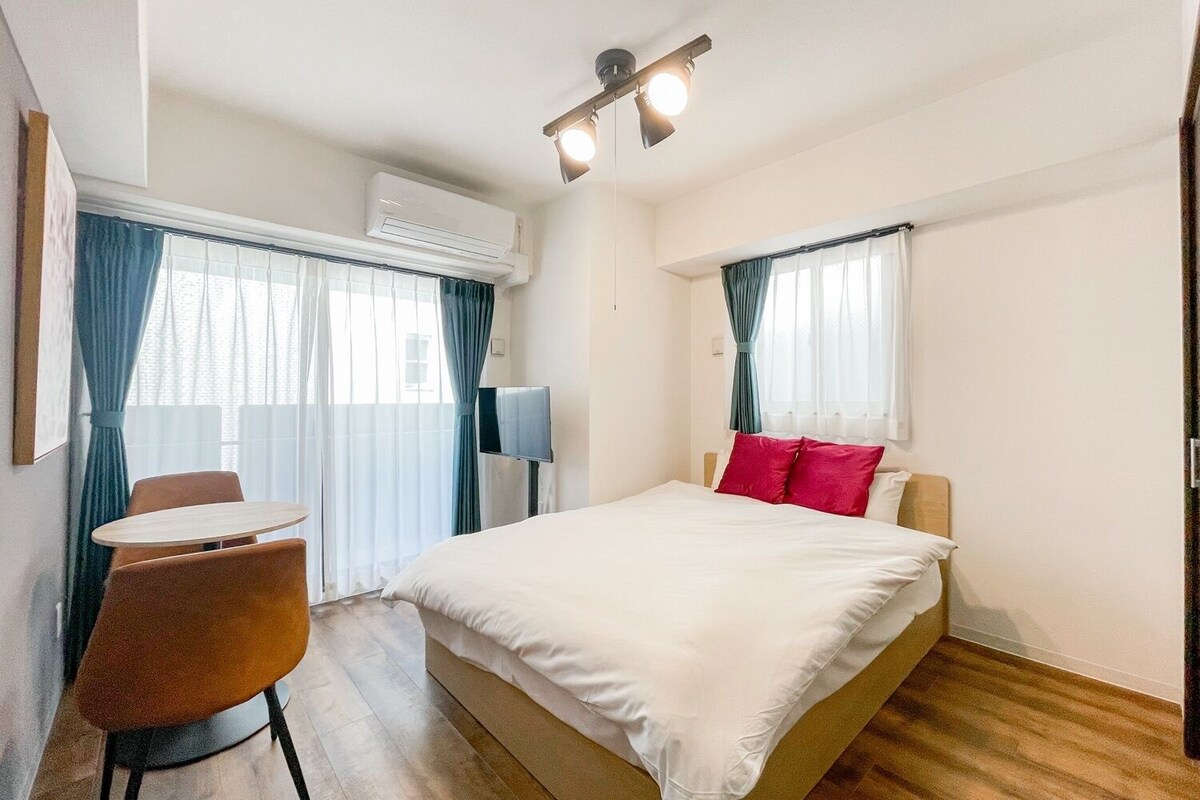 A hotel room with a bed, a desk, a chair, an air conditioning unit, and a television.